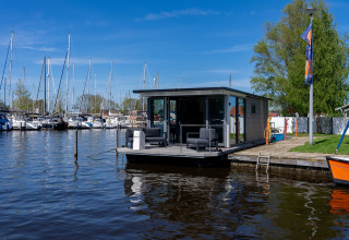 Drijvend vakantiehuis bij Marina Heeg in Friesland, Nederland, met jachthaven en zeilboten op de achtergrond.