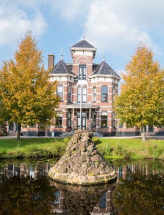 Grand historic building with a central tower, trees, and pond near Heeg, Friesland, Netherlands.