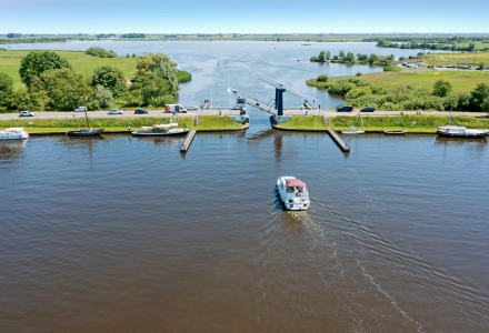 Aerial view of a boat near Heeg, Friesland, Netherlands, with a bridge, cars, and lush green landscape.