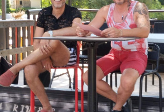Zwei Männer sitzen draußen an einem Tisch im Flower Camping La Rivière in Provence-Alpes-Côte d’Azur, Frankreich.