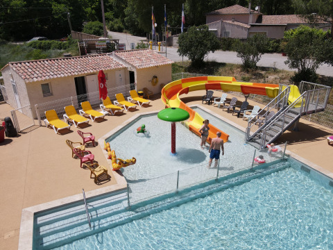 Piscina al aire libre con tobogán amarillo y tumbonas en Flower Camping La Rivière, Provenza, Francia.
