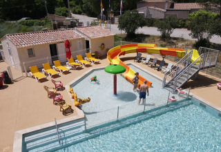 Piscina al aire libre con tobogán amarillo y tumbonas en Flower Camping La Rivière, Provenza, Francia.