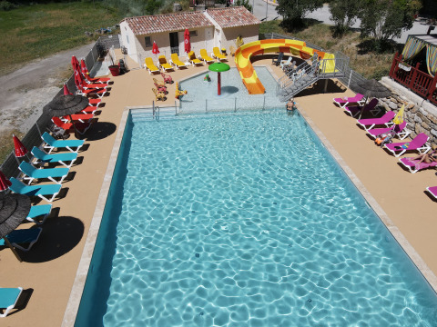 Piscina con lettini prendisole, scivolo d'acqua e ombrelloni presso Flower Camping La Rivière in Provenza, Francia.