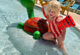 Ein kleines Kind spielt auf einer Schildkröten-Wasserspielfigur im flachen Kinderbecken eines Ferienparks.