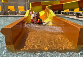 Kind mit buntem Schwimmreifen rutscht die Wasserrutsche hinunter im Flower Camping La Rivière in Frankreich.