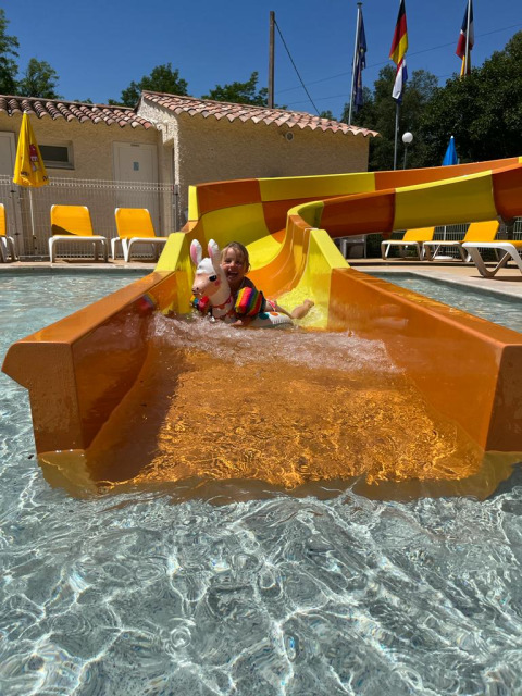 Child with a colorful float slides down a water slide at Flower Camping La Rivière holiday park in France.