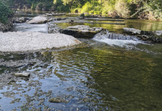 Peaceful river and gentle cascades surrounded by lush trees at Flower Camping La Rivière, Provence, France.