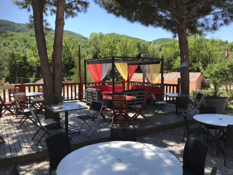 Zona de terraza al aire libre con muebles de madera y paisajes verdes en Flower Camping La Rivière, Provenza.