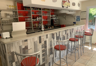 Moderno bancone bar al Flower Camping La Rivière, Provenza-Alpi-Costa Azzurra, Francia, con sgabelli rossi.