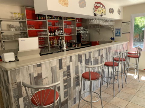 Moderno bancone bar al Flower Camping La Rivière, Provenza-Alpi-Costa Azzurra, Francia, con sgabelli rossi.