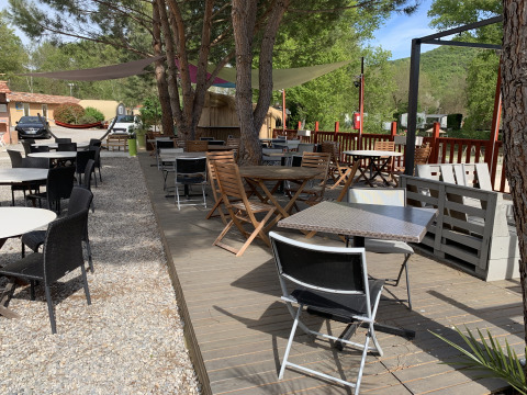 Terraza exterior con mesas y sillas bajo árboles en Flower Camping La Rivière en Provenza, Francia.