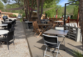 Terraza exterior con mesas y sillas bajo árboles en Flower Camping La Rivière en Provenza, Francia.
