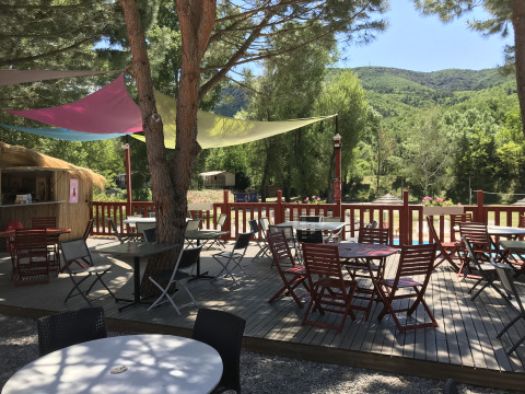 Terraza exterior con mesas y sillas bajo toldos de colores en Flower Camping La Rivière, Provenza.