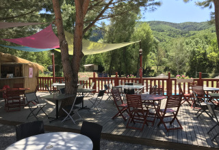 Udendørs terrasse med borde og stole under farvede solsejl på Flower Camping La Rivière i Provence.