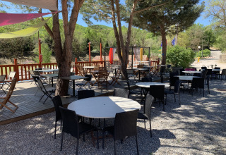 Buitenterras bij Flower Camping La Rivière met lege tafels en stoelen onder bomen in Provence, Frankrijk.