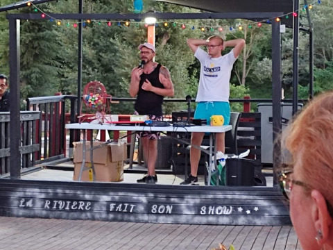 Twee mannen presenteren een evenement op het buitentoneel bij Flower Camping La Rivière in Frankrijk.