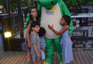 Bambini abbracciano una mascotte verde al Flower Camping La Rivière, villaggio vacanze in Provenza-Alpi-Costa Azzurra, Francia.