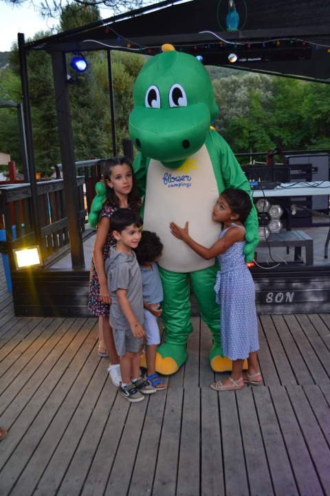 Bambini abbracciano una mascotte verde al Flower Camping La Rivière, villaggio vacanze in Provenza-Alpi-Costa Azzurra, Francia.