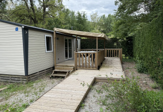Træhytte med terrasse og rampe i grønt område på Flower Camping La Rivière, Provence-Alpes-Côte d’Azur.