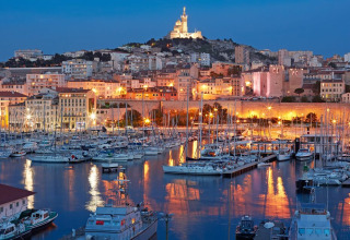 Udsigt over en lystbådehavn i skumringen med oplyste bygninger og bakker i Provence-Alpes-Côte d’Azur, Frankrig.