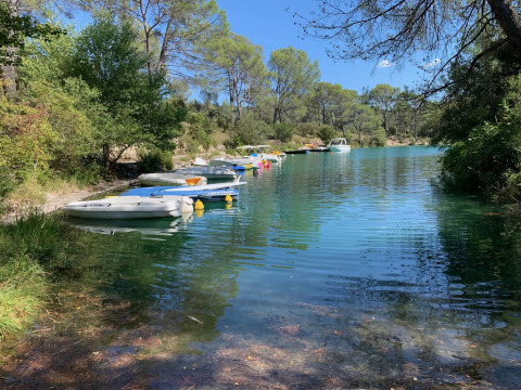Barcas atracadas en la orilla de un lago tranquilo con árboles verdes en Flower Camping La Rivière, Provenza, Francia.