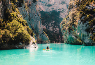 Persoon in een kajak op turquoise water tussen rotsachtige kloven bij Flower Camping La Rivière, Frankrijk.