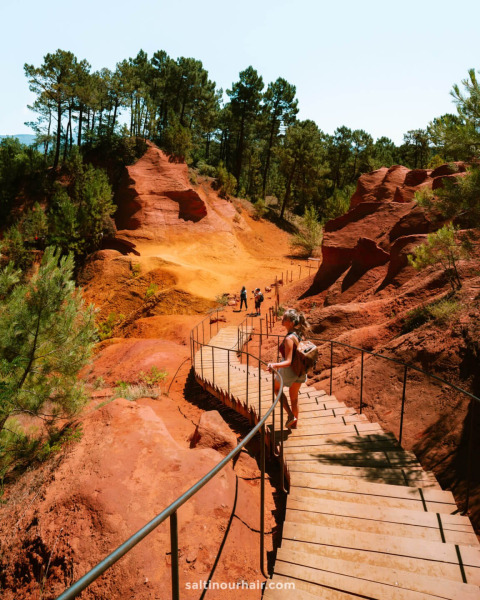Holzweg durch rote Felsen und Kiefernwald bei Flower Camping La Rivière in Provence-Alpes-Côte d’Azur.