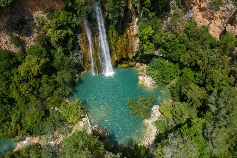 Luftaufnahme eines Wasserfalls mit türkisfarbenem Pool im Grünen im Flower Camping La Rivière, Provence.