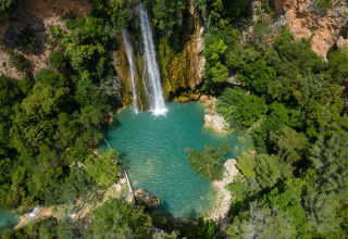 Luchtfoto van een waterval die uitmondt in een turquoise zwembad bij Flower Camping La Rivière in de Provence.