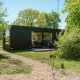 Modern black nature house at Ark Shelter, Holiday park De Klepperstee, Netherlands, surrounded by trees.