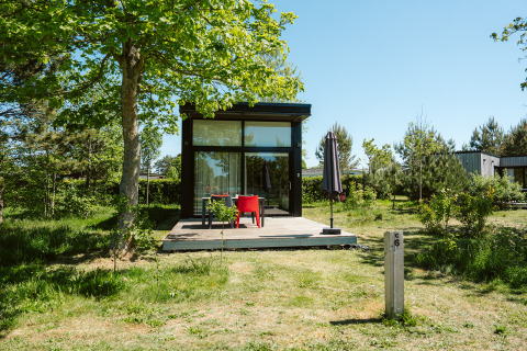 Tiny house met glazen gevel en houten terras bij De Klepperstee vakantiepark in Nederland.