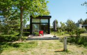 Casa pequeña con fachada de cristal y terraza de madera en el parque De Klepperstee, Países Bajos.
