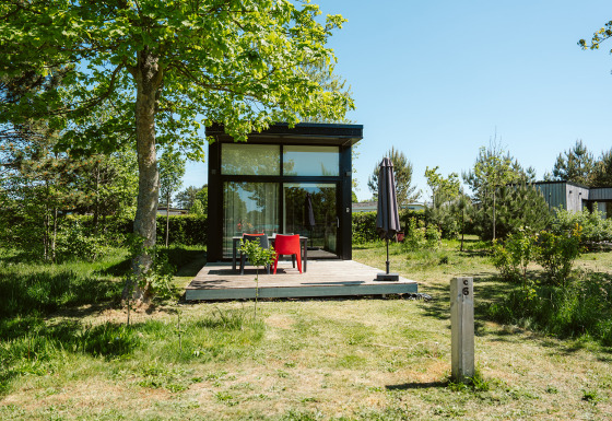 Tiny house met glazen gevel en houten terras bij De Klepperstee vakantiepark in Nederland.