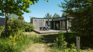 Houten natuurhuis met terras en groene tuin bij Huus van Hanse, vakantiepark De Klepperstee, Nederland.