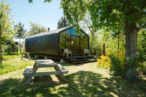 Wikkel Tiny House im Ferienpark De Klepperstee, Niederlande, umgeben von Bäumen und Picknicktisch.