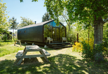 Wikkel Tiny House im Ferienpark De Klepperstee, Niederlande, umgeben von Bäumen und Picknicktisch.