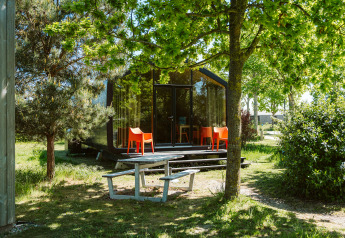 Modern natuurhuisje met grote ramen, oranje stoelen en picknicktafel in het groen bij De Klepperstee.