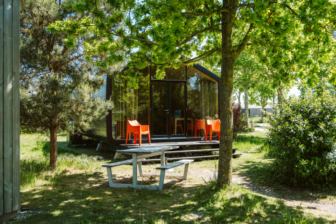 Modern natuurhuisje met grote ramen, oranje stoelen en picknicktafel in het groen bij De Klepperstee.