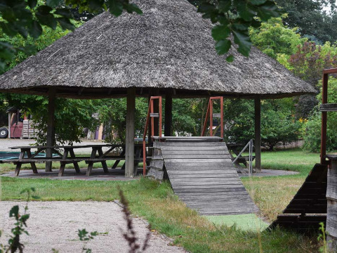 Pabellón de techo de paja con mesas de picnic y rampa de madera en Feather Down Het Boshuis, Gelderland, Países Bajos.