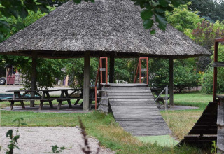 Padiglione con tetto di paglia, tavoli da picnic e rampa in legno a Feather Down Het Boshuis, Gelderland, Paesi Bassi.