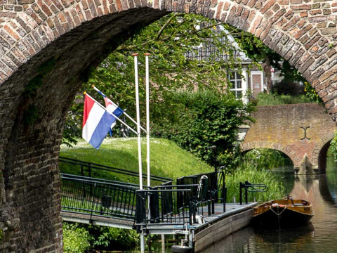 Zicht op een kanaal met aanlegsteiger, Nederlandse vlag en boogbrug in Gelderland bij Feather Down Het Boshuis.