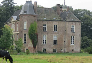 A historic brick house with towers in a green field, Feather Down Het Boshuis, Gelderland, Netherlands.