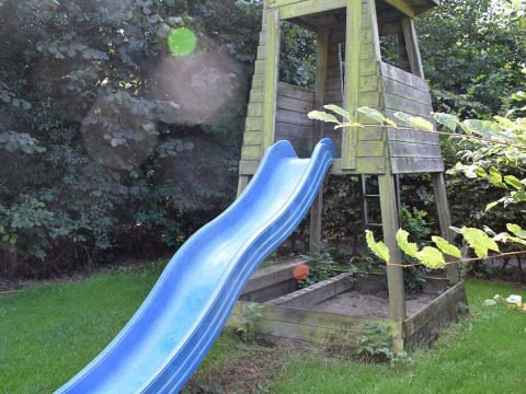 Área de juegos con tobogán azul y torre de madera en jardín verde en Feather Down Hoeve Zeeland, Zelanda, Países Bajos.