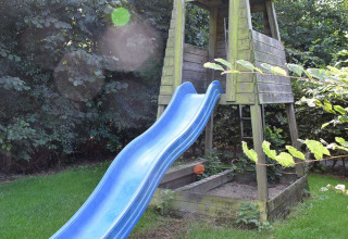 Área de juegos con tobogán azul y torre de madera en jardín verde en Feather Down Hoeve Zeeland, Zelanda, Países Bajos.