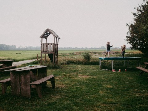 Niños jugando en una cama elástica en un jardín verde con mesa de madera en Feather Down Hoeve Zeeland, Países Bajos.