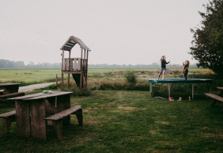 Niños jugando en una cama elástica en un jardín verde con mesa de madera en Feather Down Hoeve Zeeland, Países Bajos.