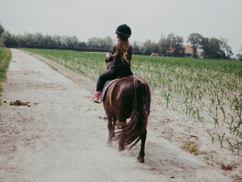 Niña montando un pony por un camino de tierra en Feather Down Hoeve Zeeland, parque vacacional en Zeeland, Países Bajos.