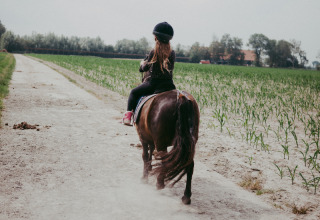 Niña montando un pony por un camino de tierra en Feather Down Hoeve Zeeland, parque vacacional en Zeeland, Países Bajos.