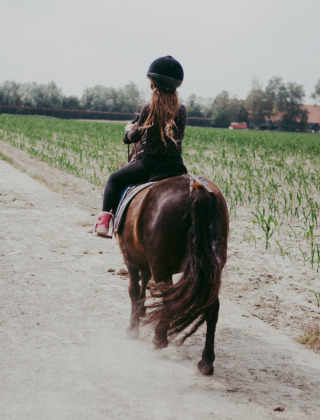 Kind rijdt op een pony over een zandweg bij Feather Down Hoeve Zeeland, een vakantiepark in Zeeland.