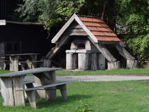 Houten picknicktafels en banken buiten, naast een bakstenen oven met pannendak, in een park in Zeeland.